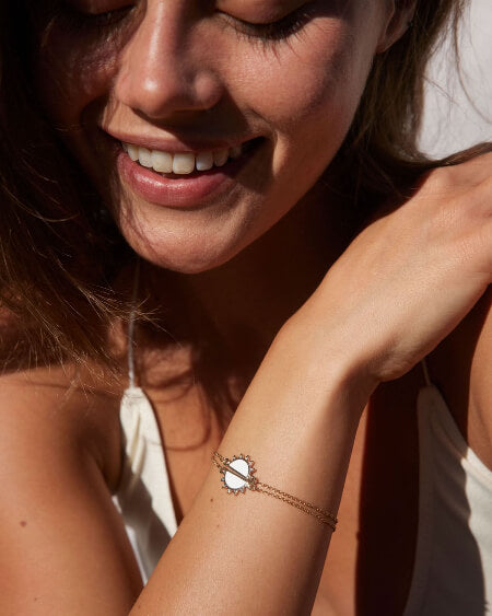 Woman wearing a bracelet with a sun design, smiling outdoors.