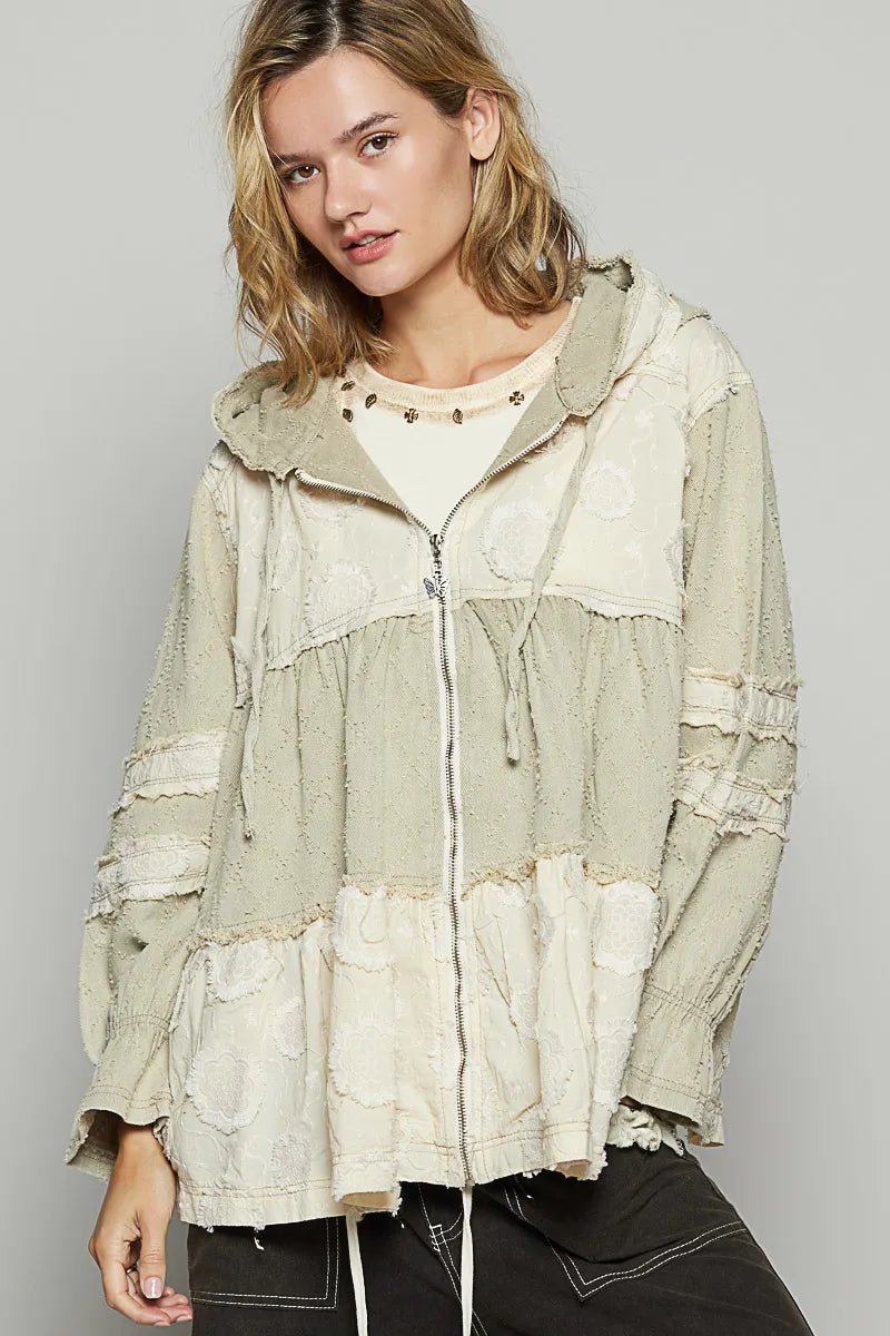 Woman wearing a light-colored hooded jacket with lace details on a plain background