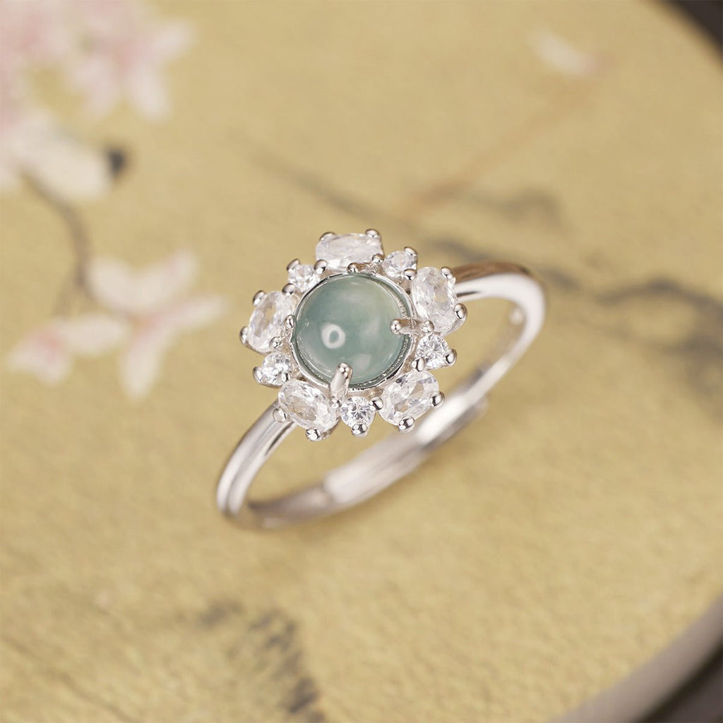 Silver ring with a green gemstone and diamond-like stones on a floral background
