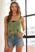 Woman wearing a green crochet top with fringes and denim shorts indoors.