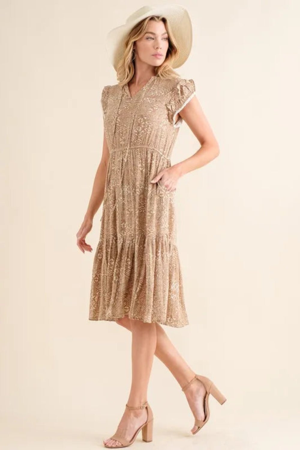 Woman wearing a beige dress and hat against a plain background