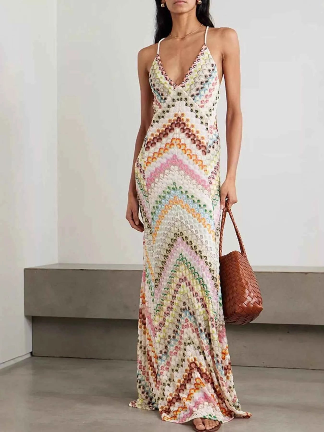 Woman wearing a colorful patterned dress holding a brown bag against a plain background