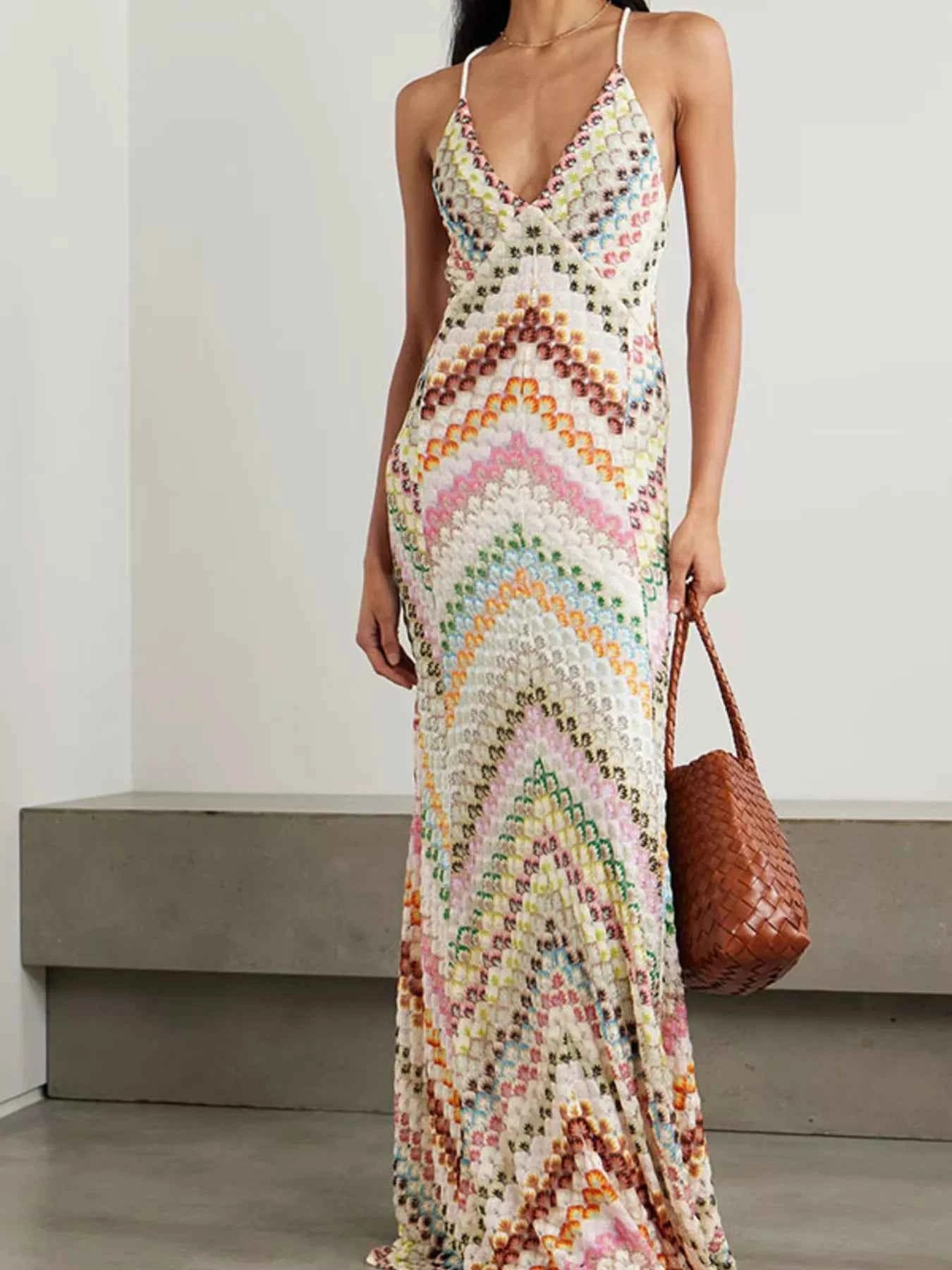 Woman wearing a colorful patterned dress holding a brown bag against a plain background