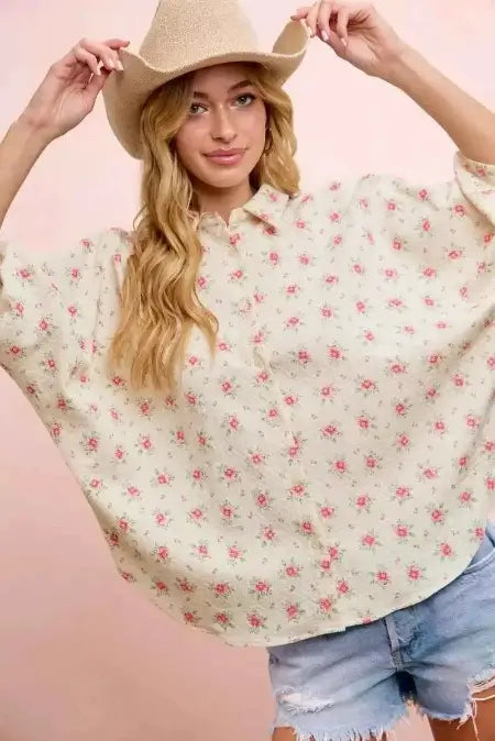 Woman wearing a floral blouse and denim shorts against a pink background
