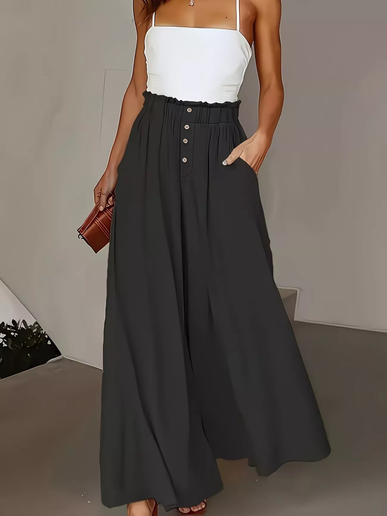 Woman wearing a white top and black wide-leg pants with a brown clutch against a neutral background