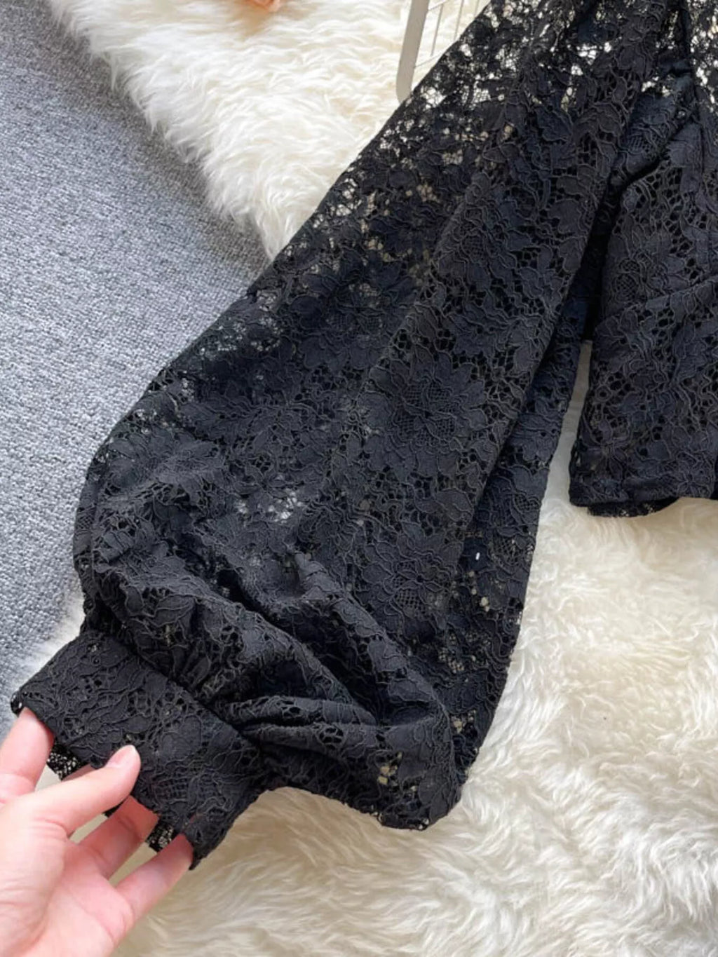 Black lace garment held by a hand on a white and gray background