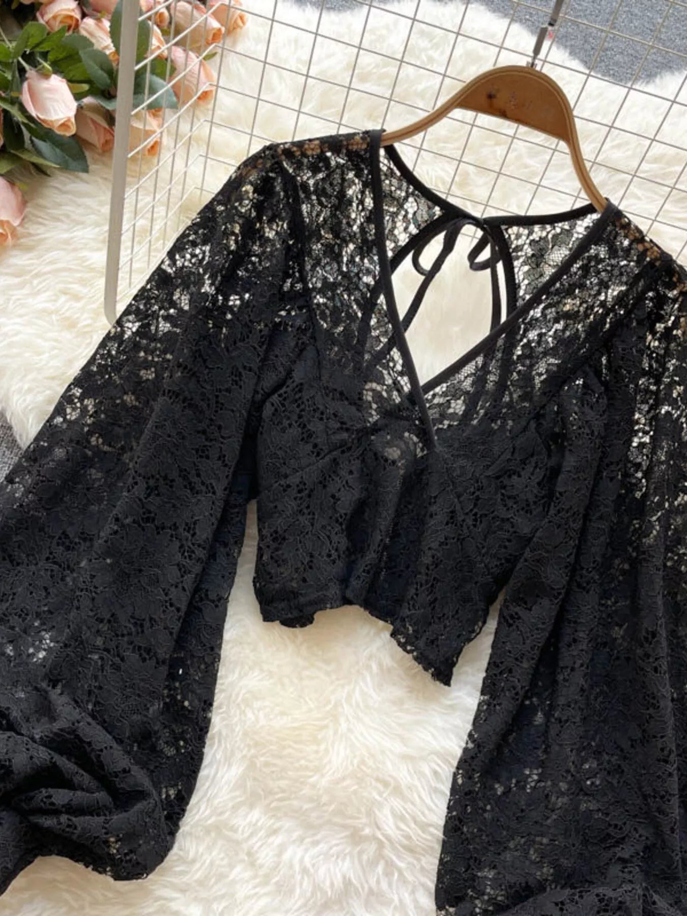 Black lace top on a hanger with a white textured surface and pink flowers in the background