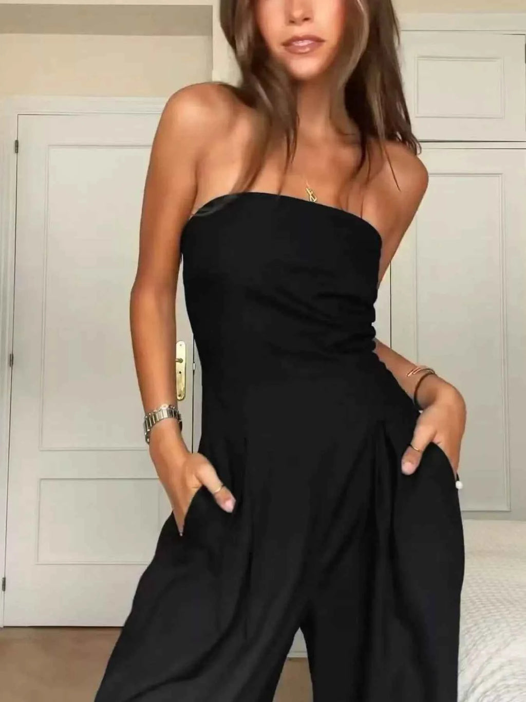 Woman wearing a black strapless jumpsuit indoors.