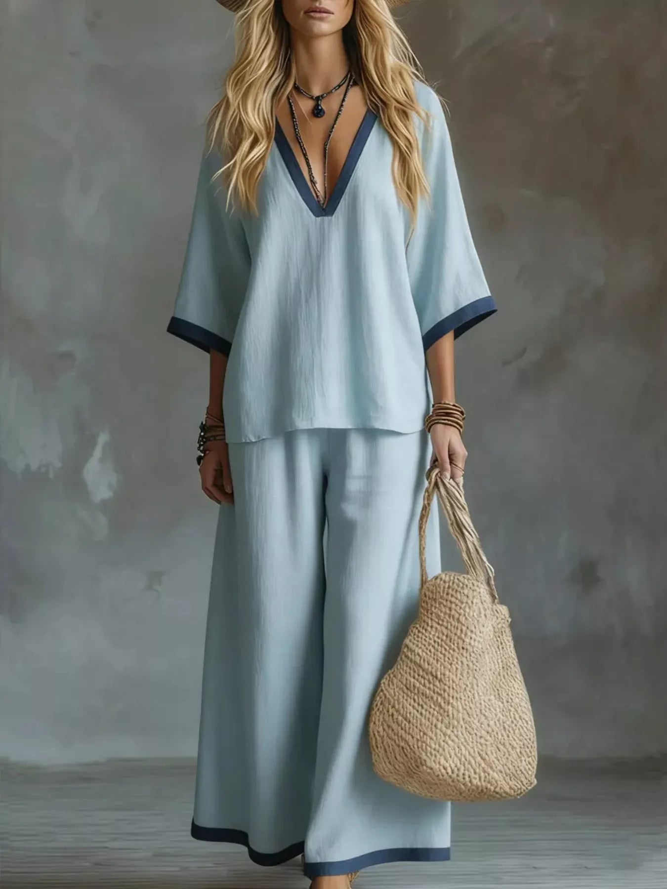 Woman in light blue outfit holding a woven bag against a neutral background