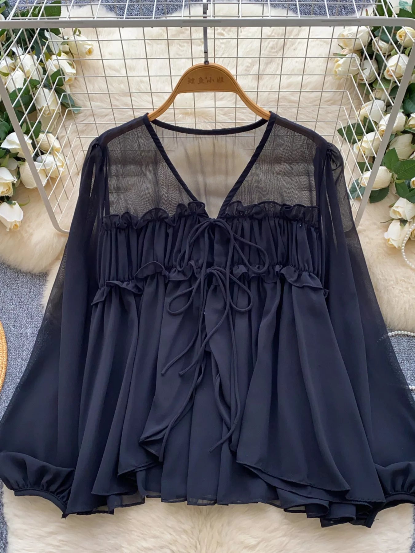 Black blouse with sheer panels on a hanger against a decorative background