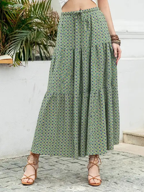 Person wearing a green patterned skirt standing outdoors with plants in the background