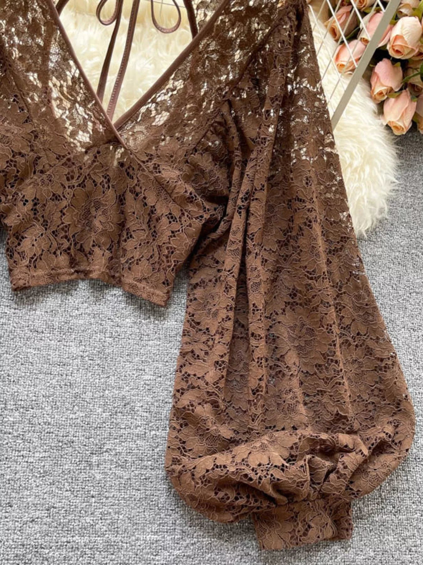 Brown lace top on a textured surface with flowers in the background