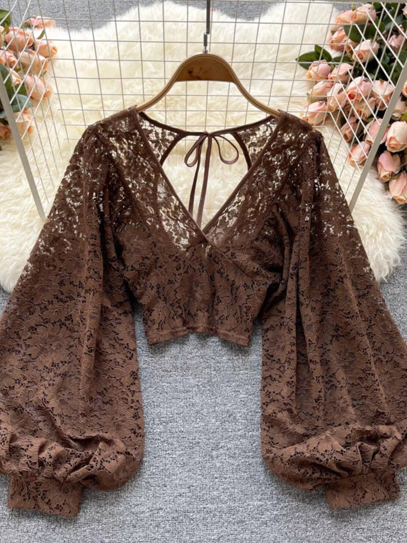 Brown lace top on a hanger with a floral background