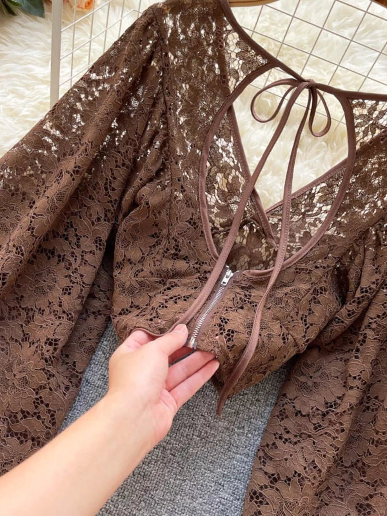 Brown lace dress with a hand holding the zipper, on a checkered floor background