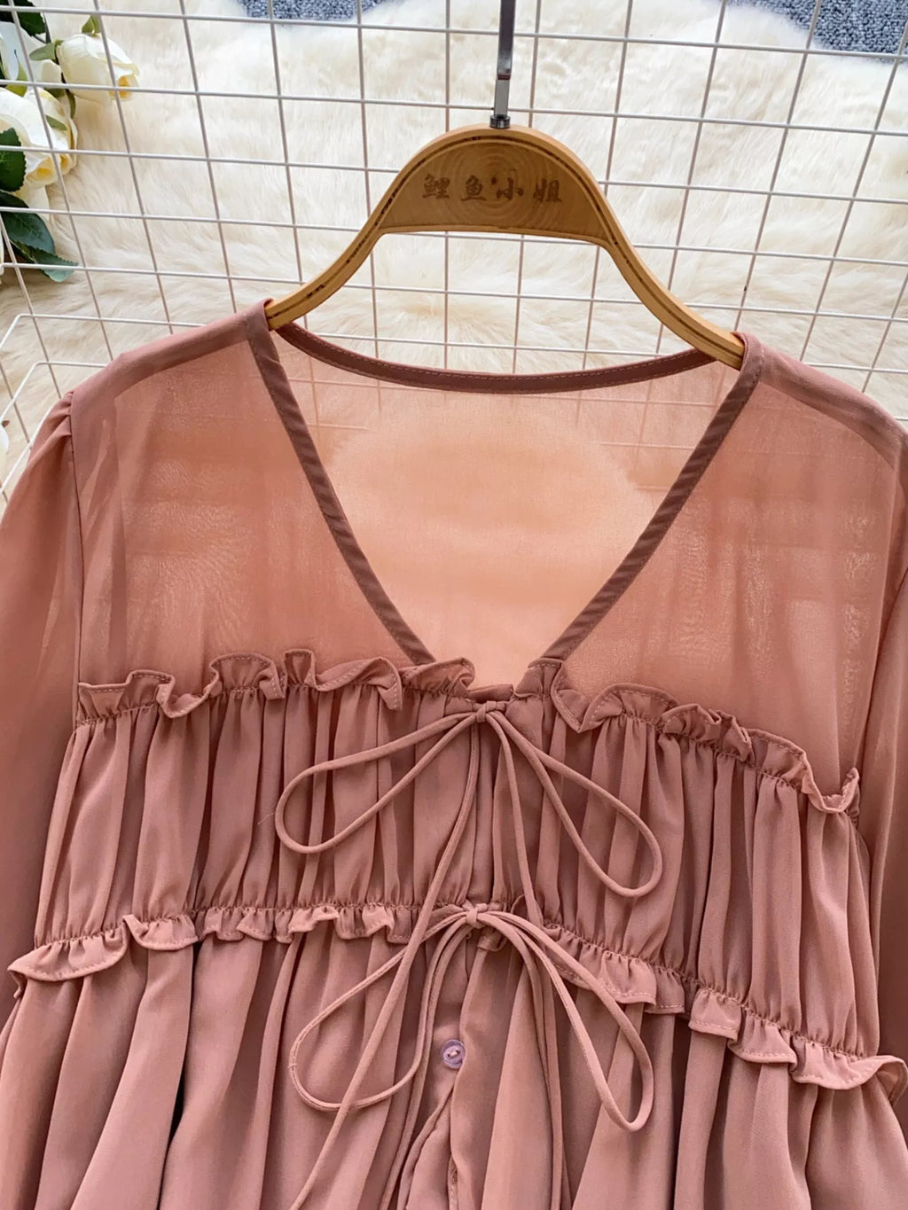 Pink dress with ruffled details on a hanger against a tiled wall background