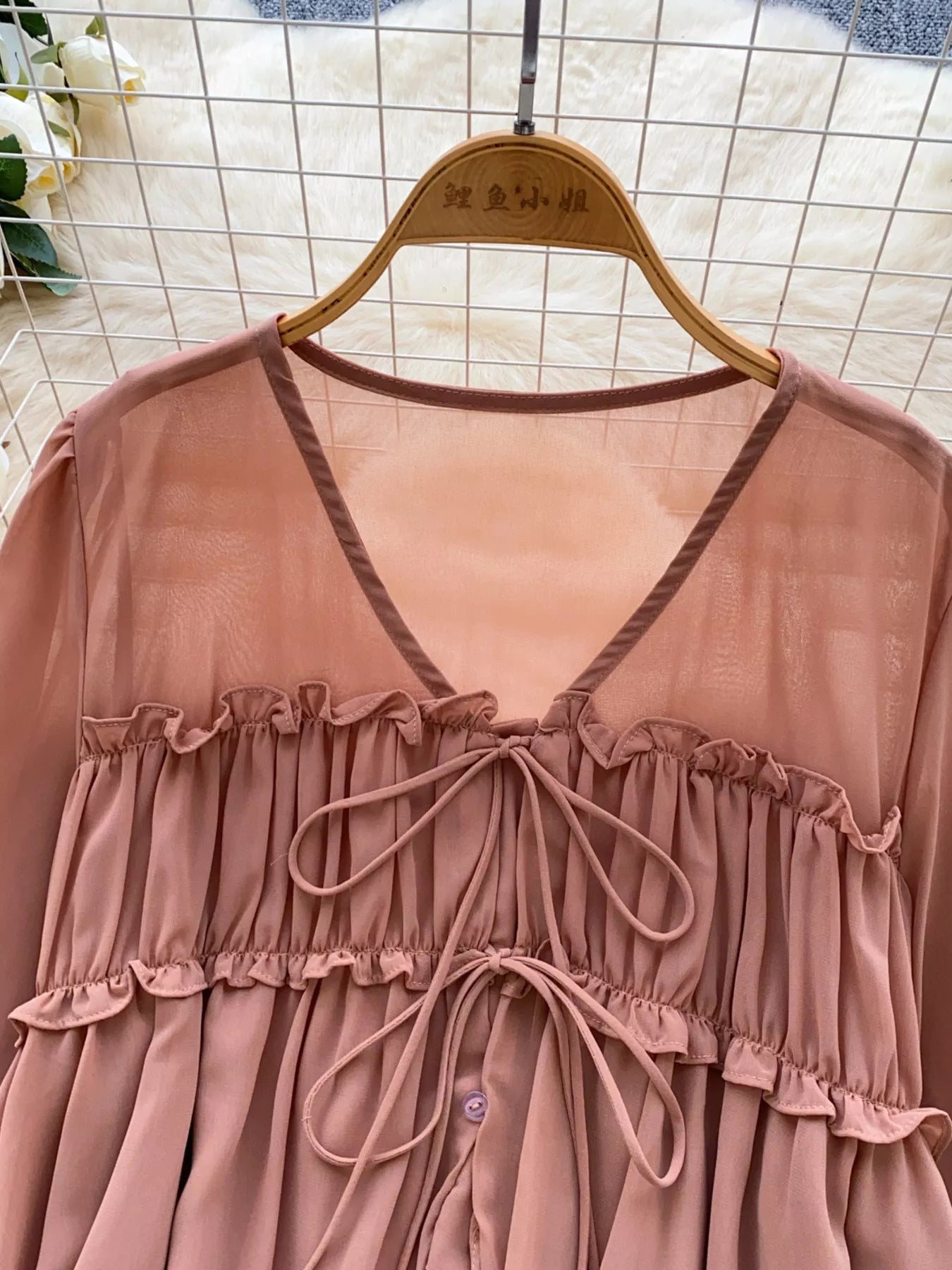 Pink dress with ruffled details on a hanger against a tiled wall background