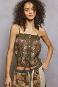 Woman wearing a floral embroidered top against a gray background