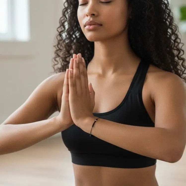 Woman in a black sports bra practicing yoga with hands pressed together.