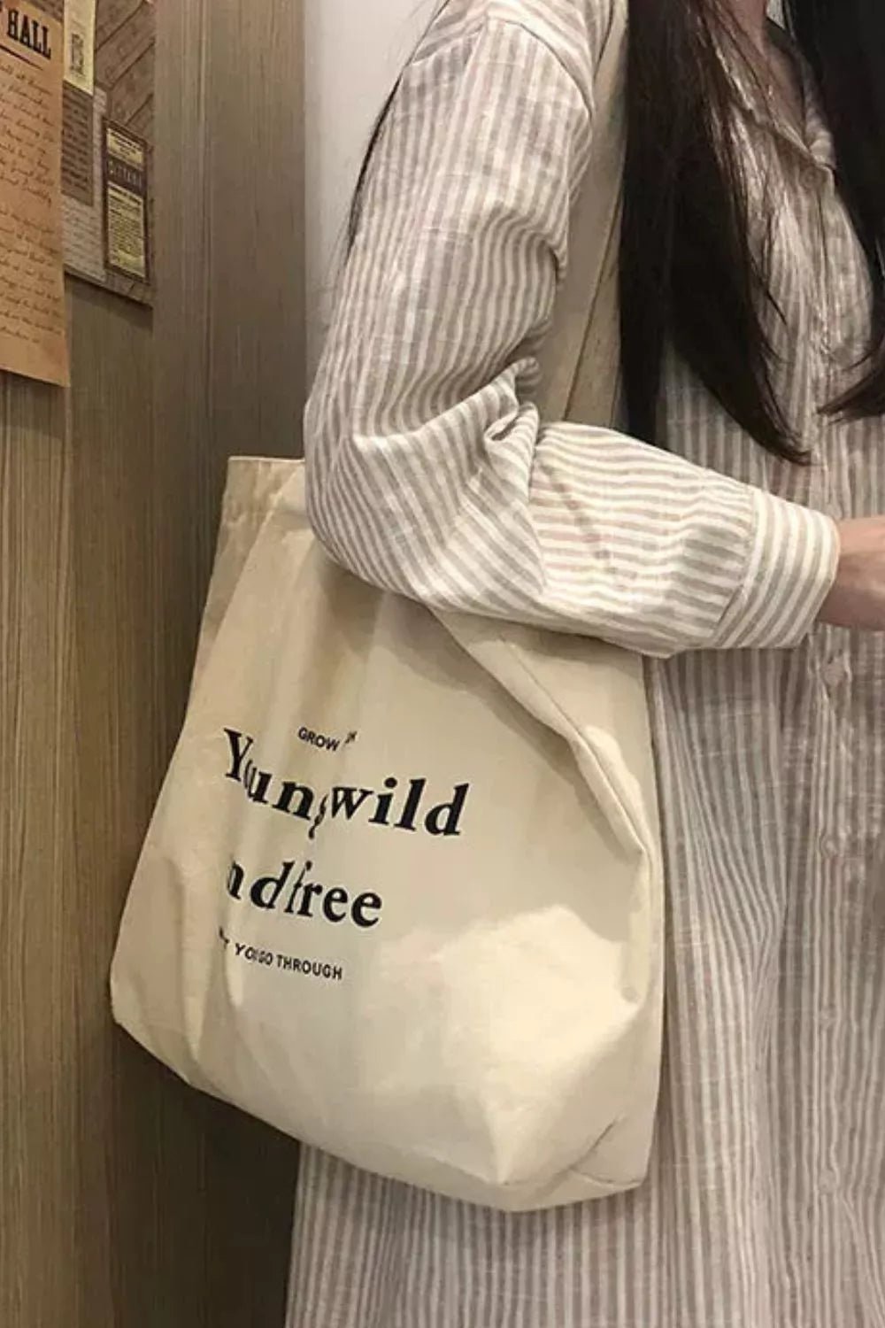 Person holding a beige tote bag with text, standing indoors.