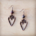 Pair of arrowhead-shaped earrings with beads on a wooden surface