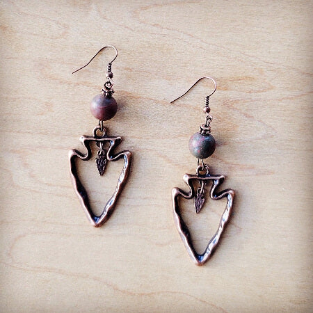 Pair of arrowhead-shaped earrings with beads on a wooden surface