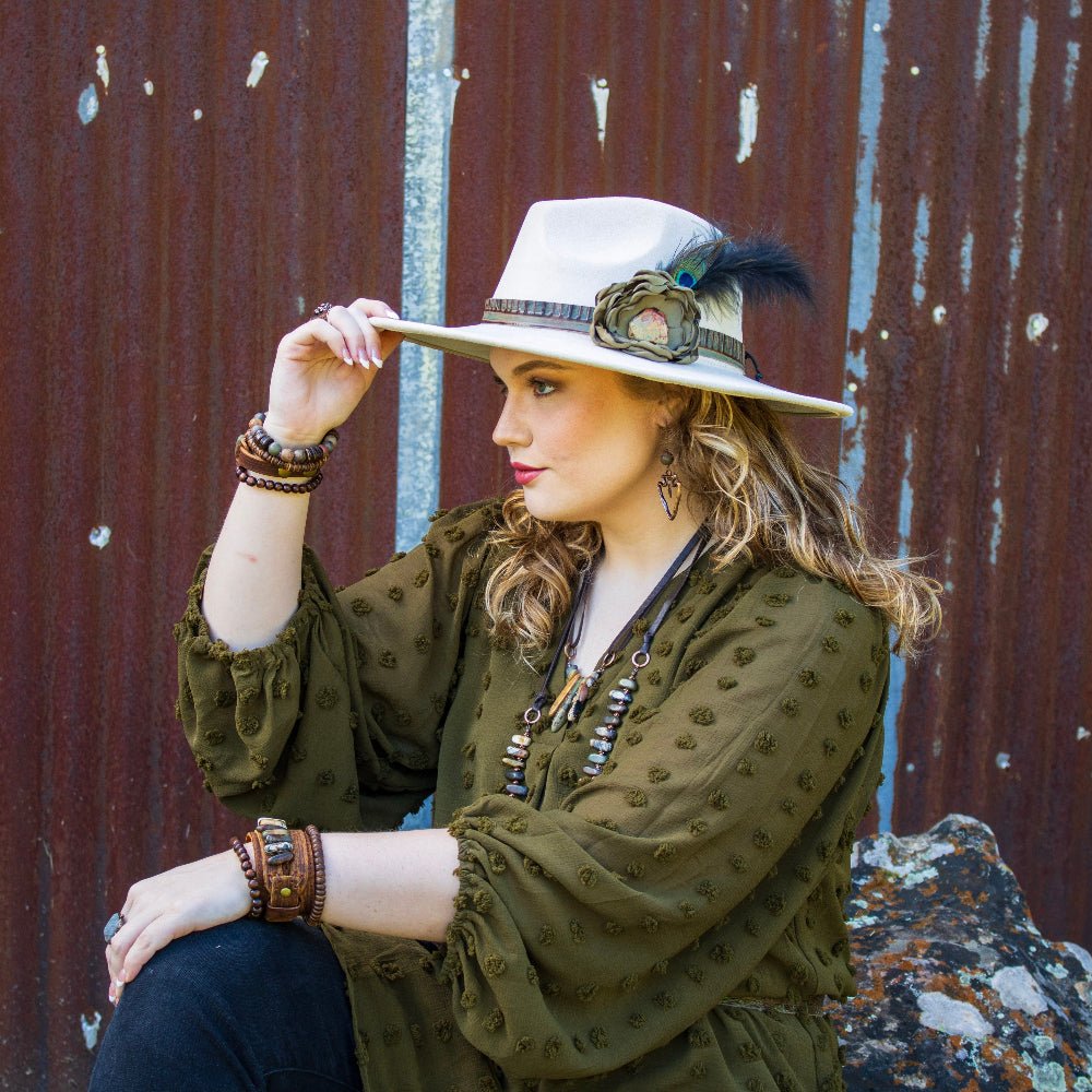 Woman wearing a wide-brimmed hat with a feather against a rustic metal wall.