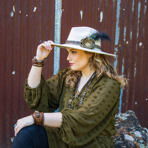 Woman wearing a wide-brimmed hat with a feather against a rustic metal wall.