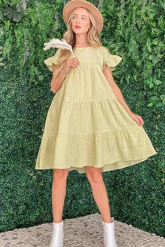 Woman wearing a light yellow dress and beige hat against a green leafy background