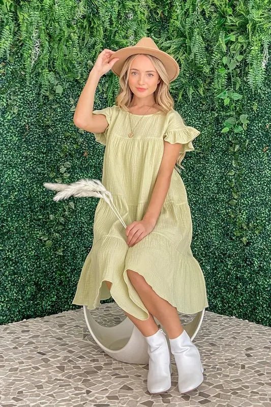 Woman in a light green dress and white boots standing against a green leafy background