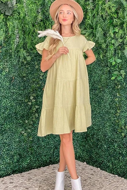 Woman wearing a light yellow dress and white boots against a green leafy background