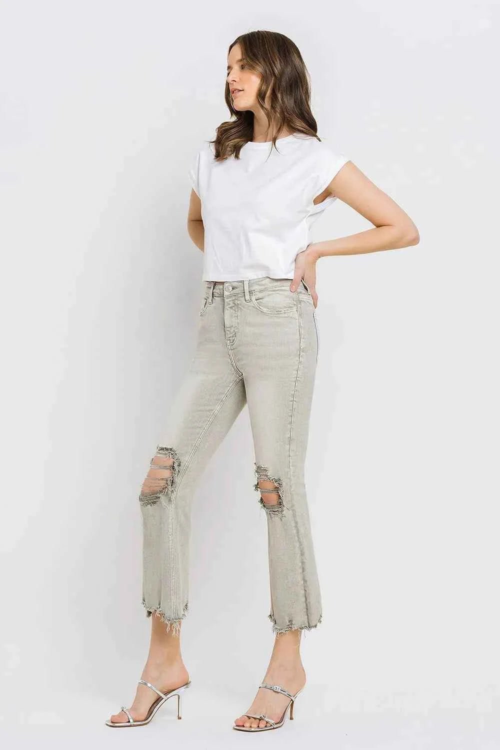 Woman wearing light gray distressed jeans and a white top sideways on a white background