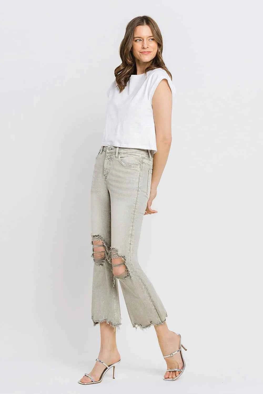 Woman wearing a white sleeveless top and light gray distressed jeans on a white background