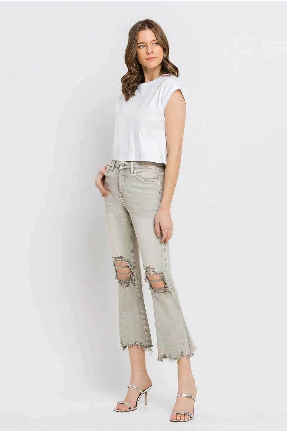 Woman wearing a white sleeveless top and light gray distressed jeans on a white background
