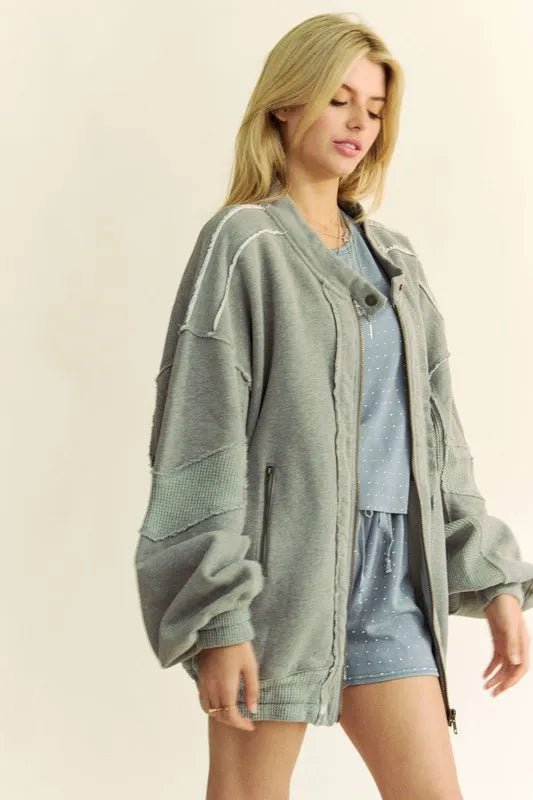 Woman wearing a gray oversized jacket over a blue top and shorts on a beige background