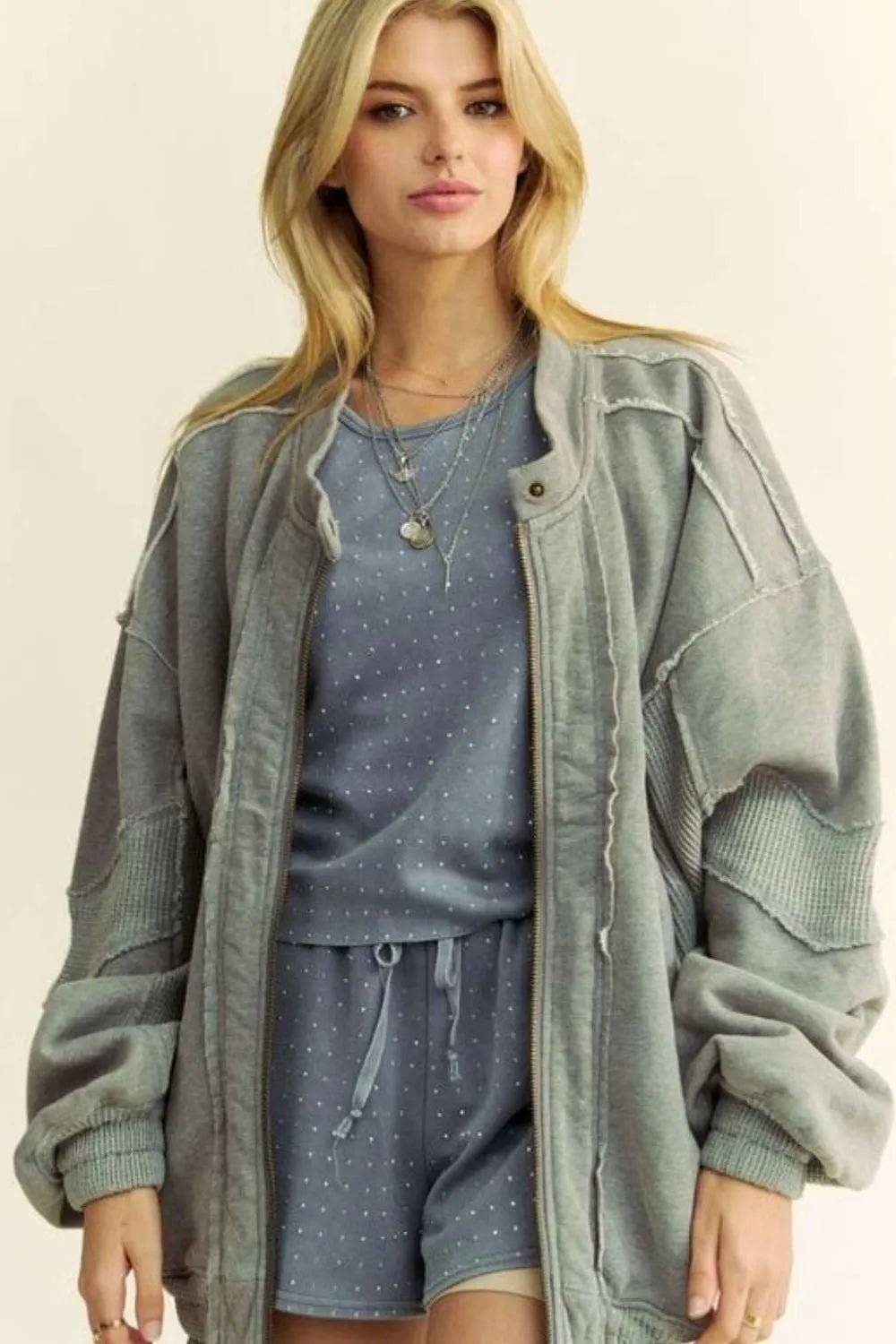 Woman wearing a green jacket over a blue outfit with a beige background