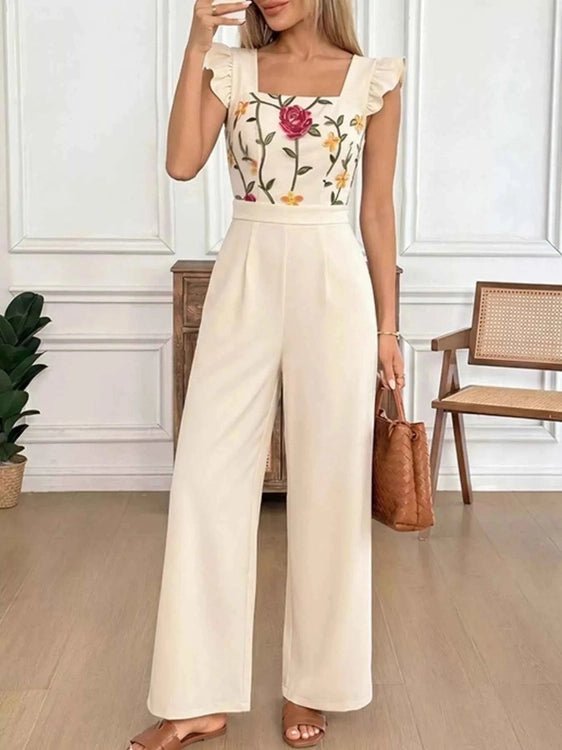 Woman wearing a floral top and beige wide-leg pants in an indoor setting.