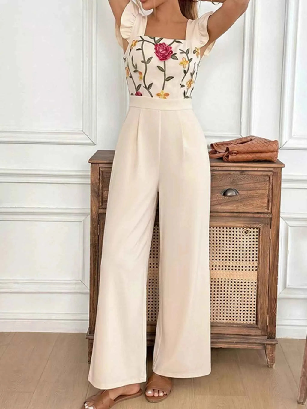 Woman wearing a floral top and beige wide-leg pants in a room with wooden furniture.