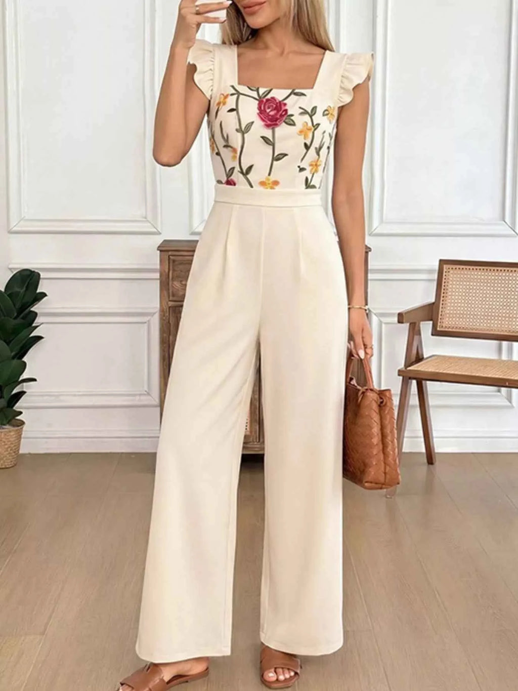 Woman wearing a floral top and beige wide-leg pants in an indoor setting.