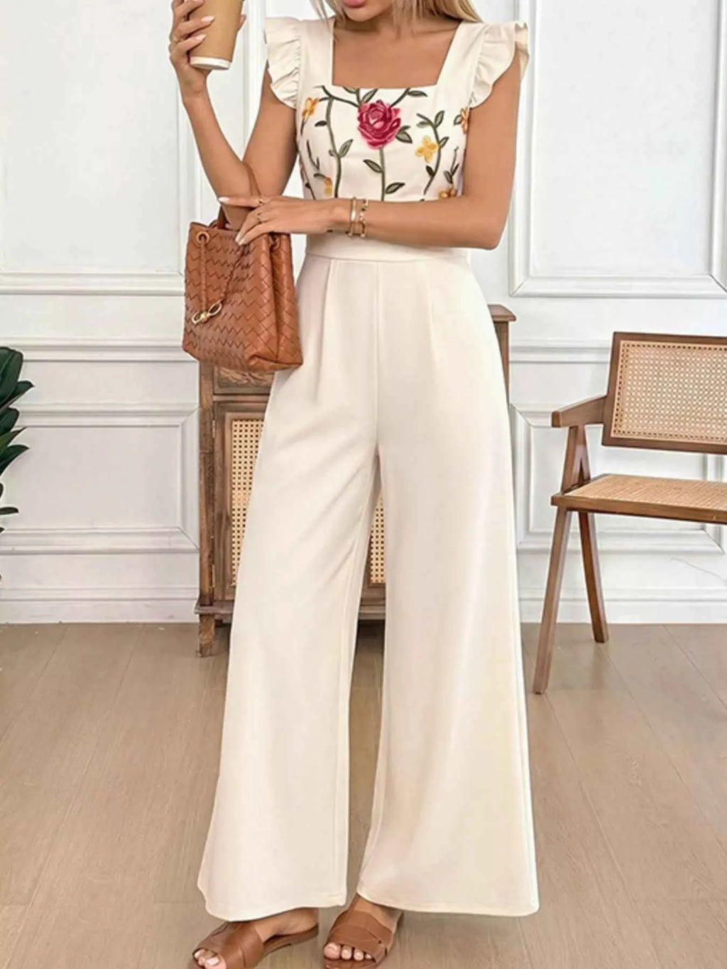 Woman wearing a floral top and white wide-leg pants in an indoor setting.
