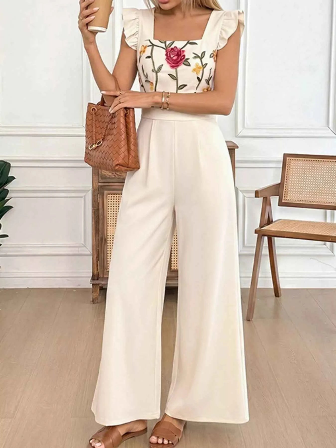 Woman wearing a floral top and white wide-leg pants in an indoor setting.