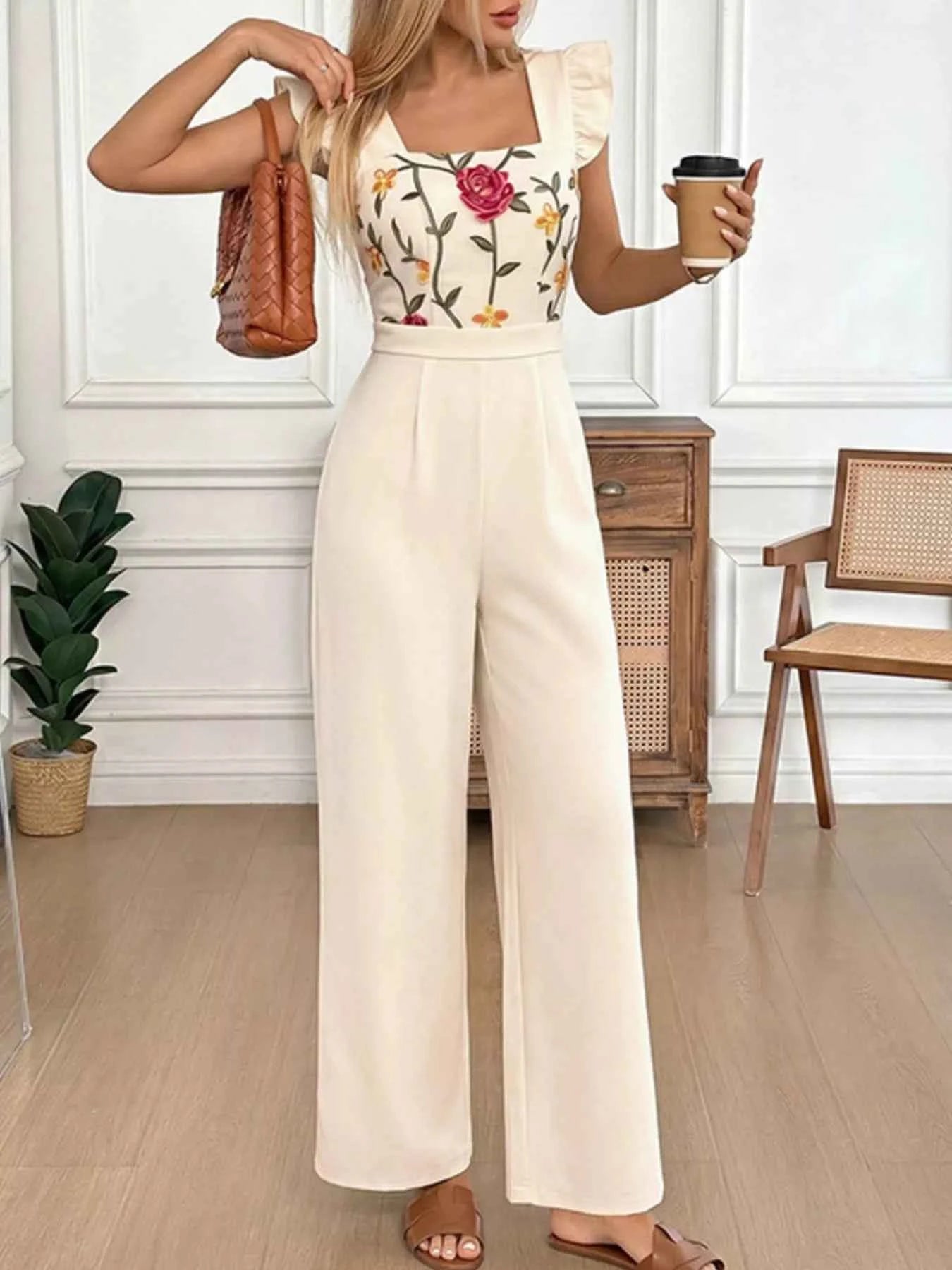 Woman in floral top and wide-leg pants holding a coffee cup indoors.