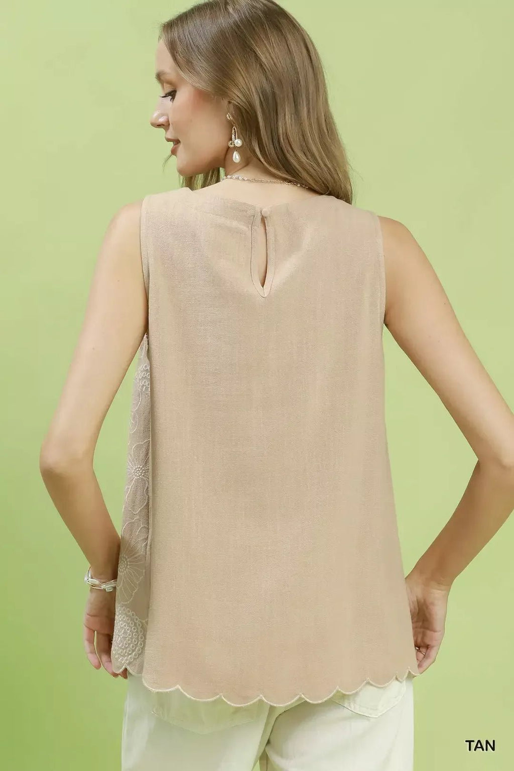 Woman wearing a beige sleeveless top against a light green background
