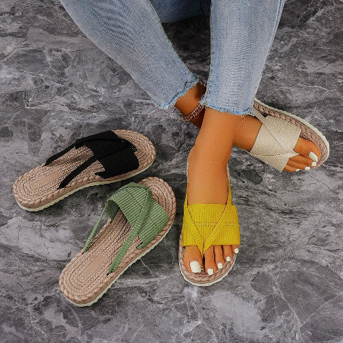 Two pairs of sandals on a stone floor, one with a yellow strap and the other with a green strap.