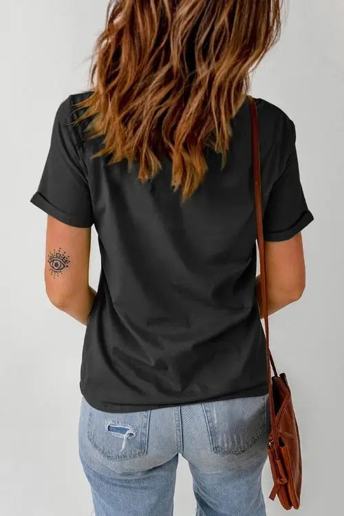 Person wearing a black t-shirt and blue jeans with a tattoo on their arm, standing against a plain background.