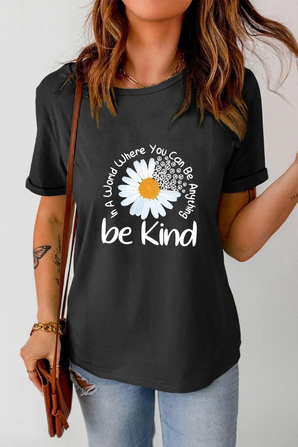 Person wearing a black t-shirt with a daisy graphic and 'be kind' text.