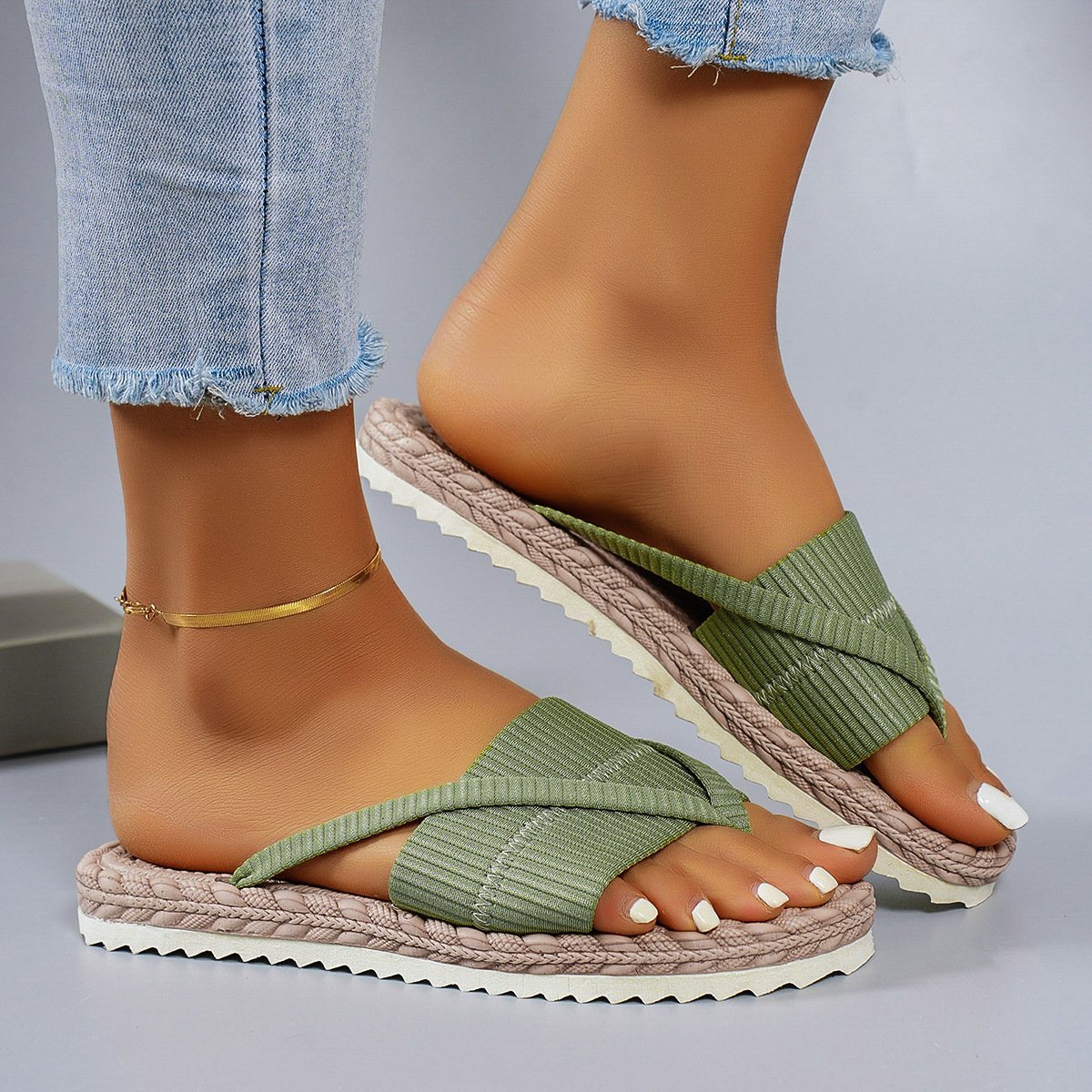 Green sandals with woven straps worn by a person on a gray background