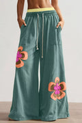 Green pants with floral patches worn by a person on a neutral background