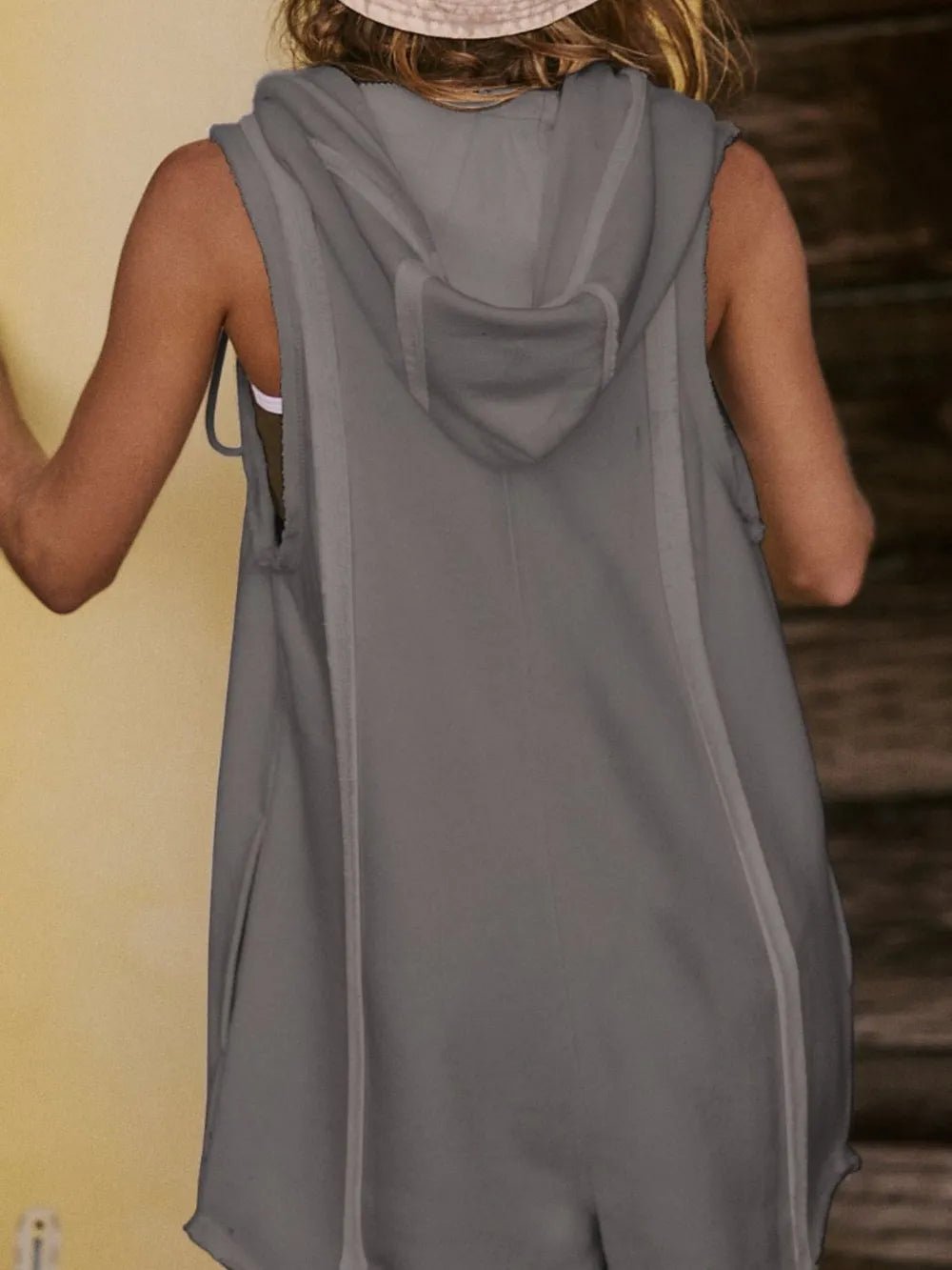 Person wearing a gray sleeveless hoodie with a hood, standing against a neutral background.
