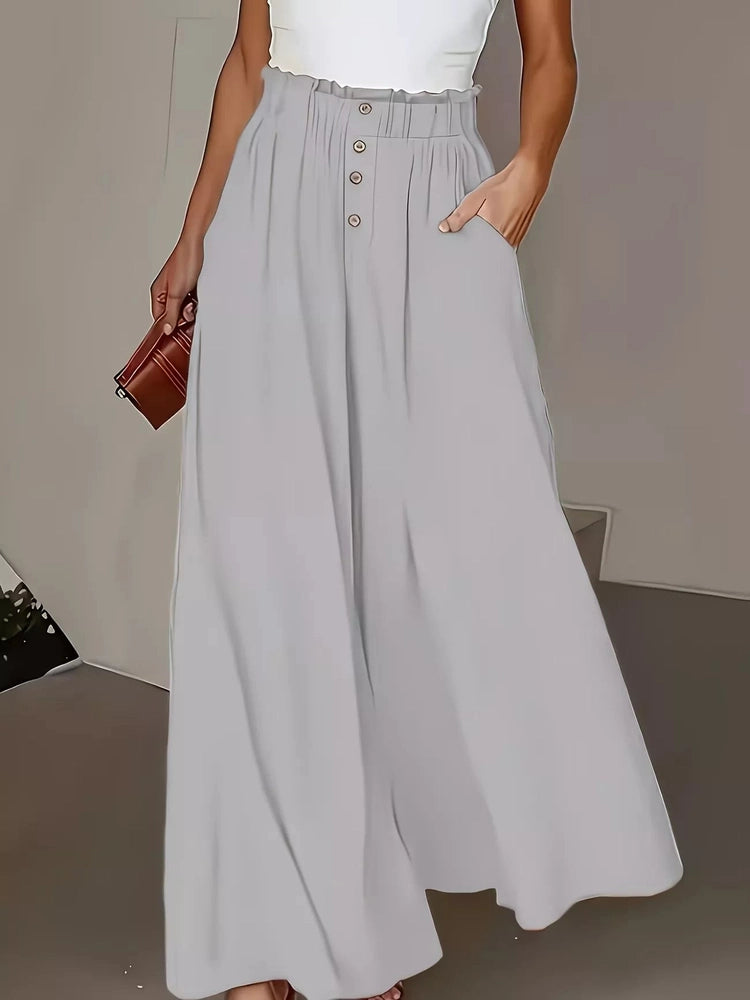 Person wearing light gray wide-leg pants with a white top and brown clutch against a neutral background