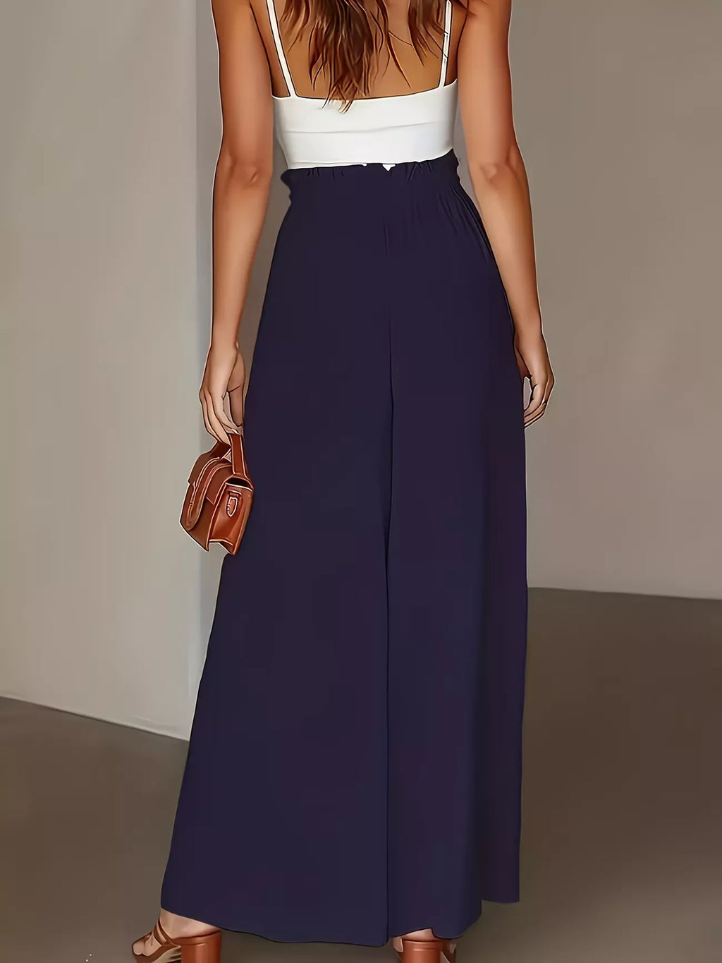 Woman wearing a white top and navy blue skirt holding a brown handbag against a neutral background